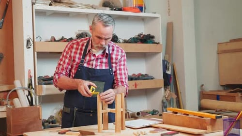 Senior Carpenter Uses Tape Measure to Measure Wooden Slats for Project Ensuring Precision in Each