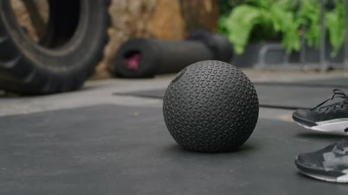 Active Woman in Fitness Gear Performs Slam Ball Exercises at Outdoor Gym Surrounded By Rich Plants