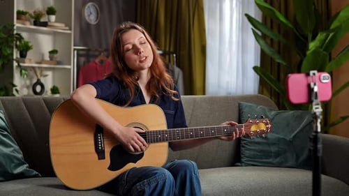 Girl Sits, Plays Acoustic Guitar, and Sings in Home