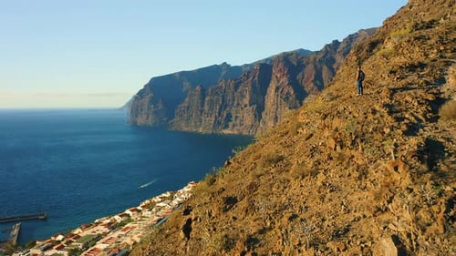 Man Backpacker Stands on Mountain Top Ocean Coast at Sunset