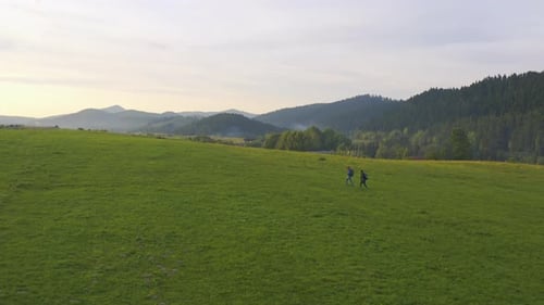 Hikers Walking Across Green Field at Sunset