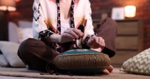 Woman playing steel tongue drum on floor at home, closeup
