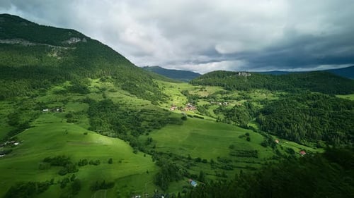 Aerial Hyperlapse Over Green Hills Forests and Rural Village Under Cloudy Sky