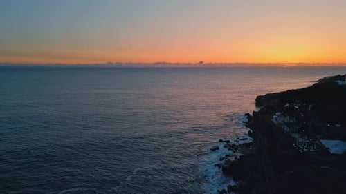 Sunset drone view of tranquil ocean waves washing rocky seashore in summer evening