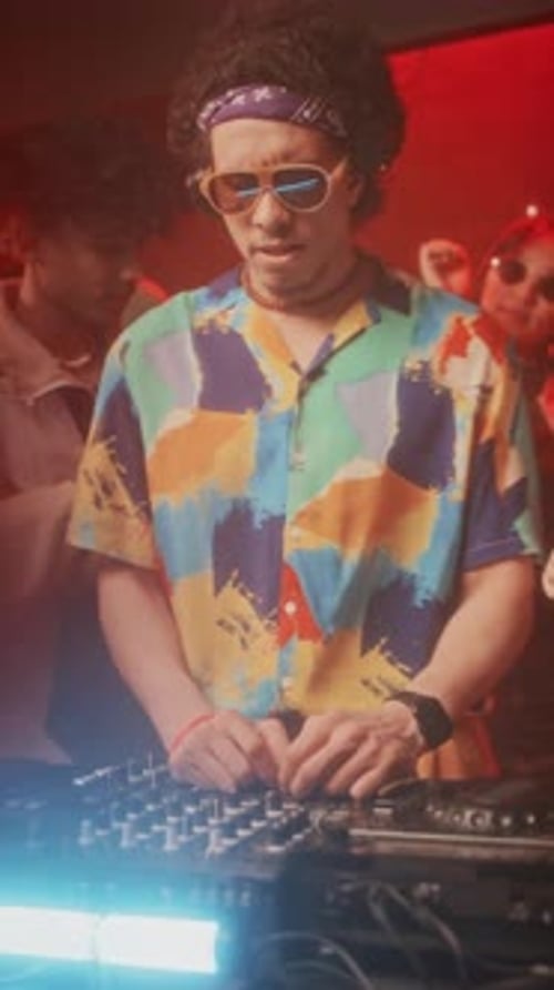 Vertical of Cool Hipster-Like DJ Amusing Crowd during Rave Party in Club