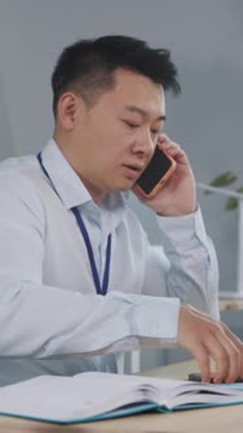 Man Talking on Two Phones in Office Setting
