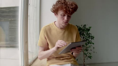 Young Adult Using Tablet by Window