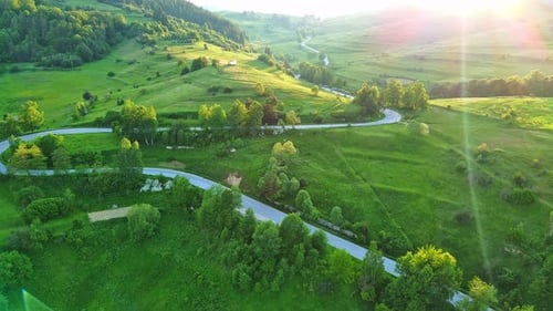 A Road Passes Hills Covered with Spruce Forests and Meadows Against a Cloudy Sky