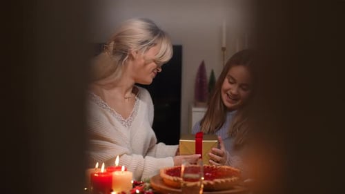 Woman Giving Gift to Child at Christmas Dinner