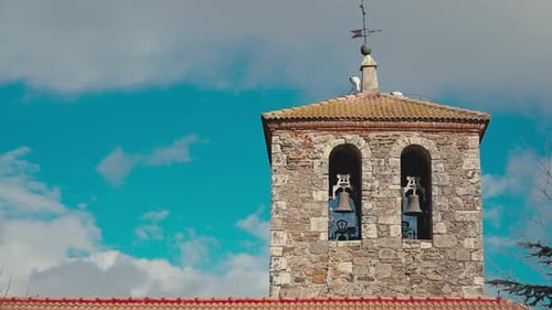 Bell Tower on the Right in Sunshine with White and Black Stork Making Nest As Sun Hiding Behind