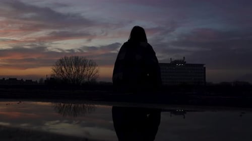 Dramatisch Silhouettenaufnahme eines Mädchens, das auf einer Dachkante sitzt, während die Sonne untergeht (Zeitlupe)