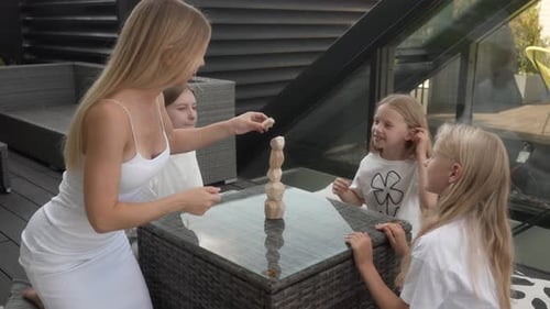 Family Fun: Mother & Daughters Build and Topple Wooden Block Tower on Rooftop