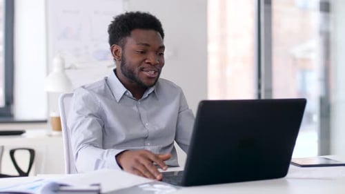 Happy Young Man Video Conferencing on Laptop at Desk