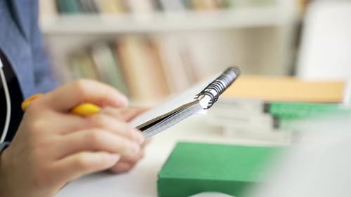 Close up. A female hand writes with a pen in a notebook at the university library. Student taking