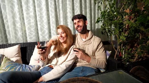 Glückliches Paar entspannt sich auf dem Sofa, trinkt Wein und schaut Film