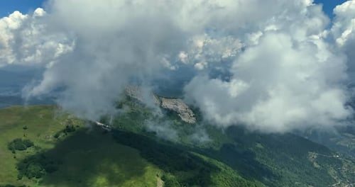 Flying trough white fluffy clouds above green mountain peaks. Beautiful summer sunny day on the high