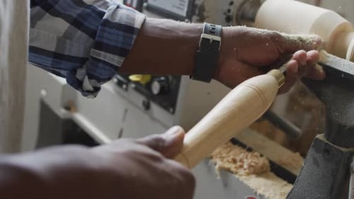 Close up of african american male carpenter hand's turning wood on a lathe at carpentry shop