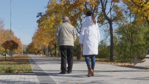 Back View of Elderly Man and Caregiver in Park Autumn Nursing Care