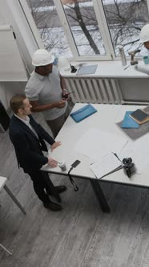 Three Specialists Reviewing Blueprints on Table in Construction Office