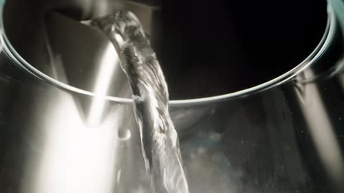 Boiling water is poured into a glass from a metal kettle, super macro view inside the glass. Steam.