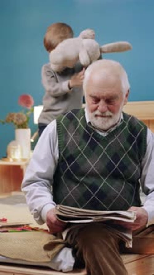 Grandfather Reads Newspaper as Grandchild Plays