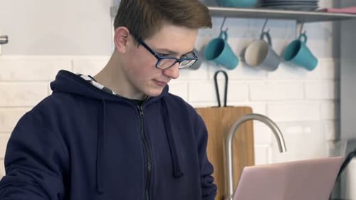 Teen using laptop in kitchen, typing, indoors