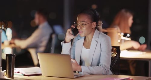 Businesswoman on Laptop Talking on Phone in Office at Night