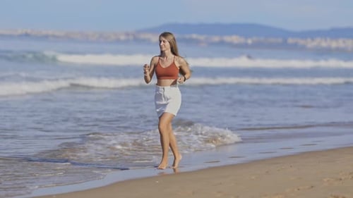 Energetic Young Woman Sprinting Along the Sunlit Beach Shoreline