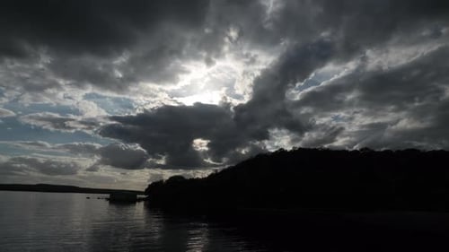 4k time lapse sunset over lake and small mountain with multiple clouds in the blue skies.