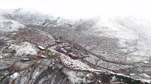 Aerial establishing overview of Larung Gar Tibetan Buddhist academy and town covered in snow, TIbet,
