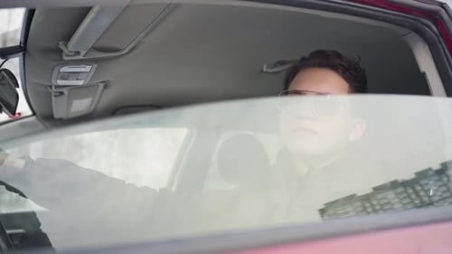 Boy in Winter Jacket Rolling Down Car Window with Building Reflection on Glass
