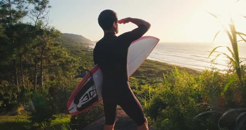 Surfer with board. Surfer in black wetsuit stands on the grass holds the surf board and checks the w