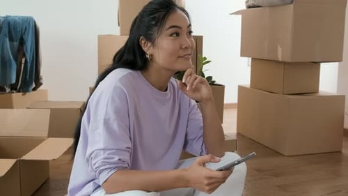 Woman with Phone Sits Surrounded by Moving Boxes