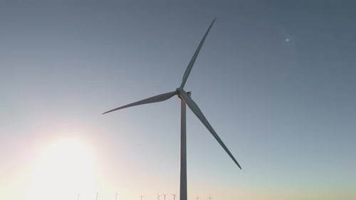 Wind Turbine Spinning Against Sky At Sunrise. - aerial tilt down shot