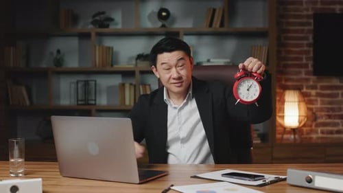 Glücklicher asiatischer Mann posiert vor der Kamera mit Wecker bei der Arbeit