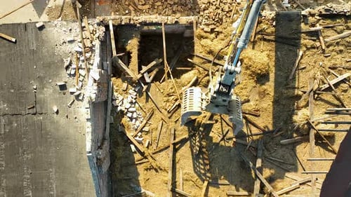 Vue aérienne d'une griffe d'excavatrice déchirant une structure de plancher, avec des débris et du bois éparpillés