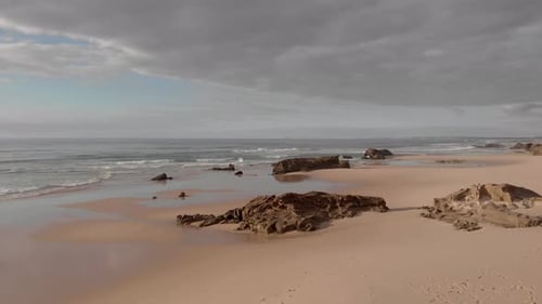 Rocky outcrops on pristine sandy beach backed by coastal cliffs; aerial pan