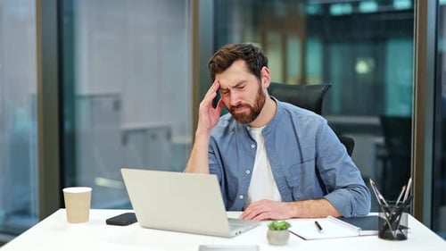 Stressed Businessman with Headache Working on Laptop in Modern Office