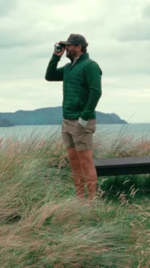 Vertical shot of male golfer standing in rough using range finder to get accurate yardage to pin on