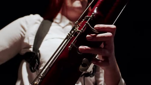 Female Musician Plays Classical Music on Bassoon While Sitting on Chair in Studio Dark Background