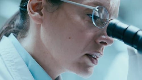 Female Lab Scientist Using Microscope and Talking in Research Center