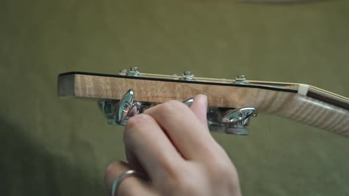 Guitarist Tuning The Acoustic Guitar By Turning The Machine Heads Or Tuning Pegs On The Headstock. -