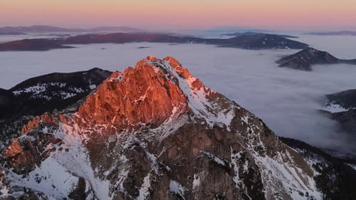 Aerial View of Snowy Rocky Peaks Illuminated By Sunset Light with Fog Draping the Valley Below FHD