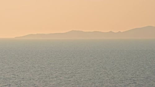 Seascape at sunset with mountain in background. Static shot