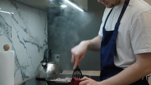 Blond Man Cooking Meat in Pan in Kitchen