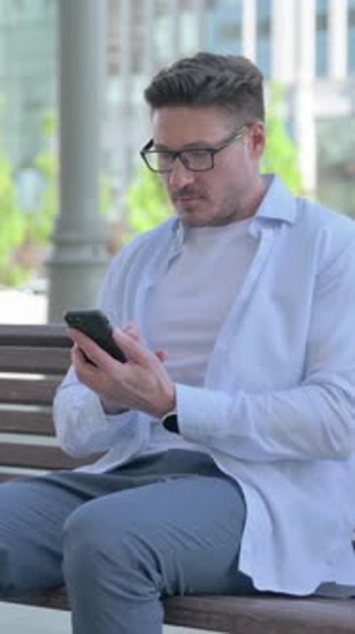 Man On Bench Using Smartphone in Urban Setting