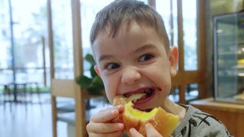 Happy Child Eats a Bun with Jam and Cottage Cheese in a Cafe