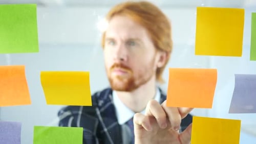 Redhead Businessman Working On Sticky Notes Attached on Glass in Office
