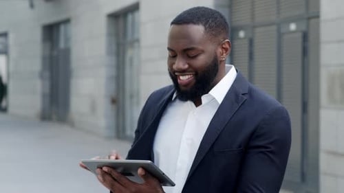 Happy african american businessman typing message on digital tablet at city street