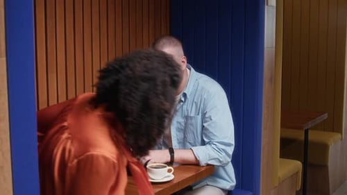 Woman Sitting down at Table to Male Coworker Using Laptop in Modern Office Space